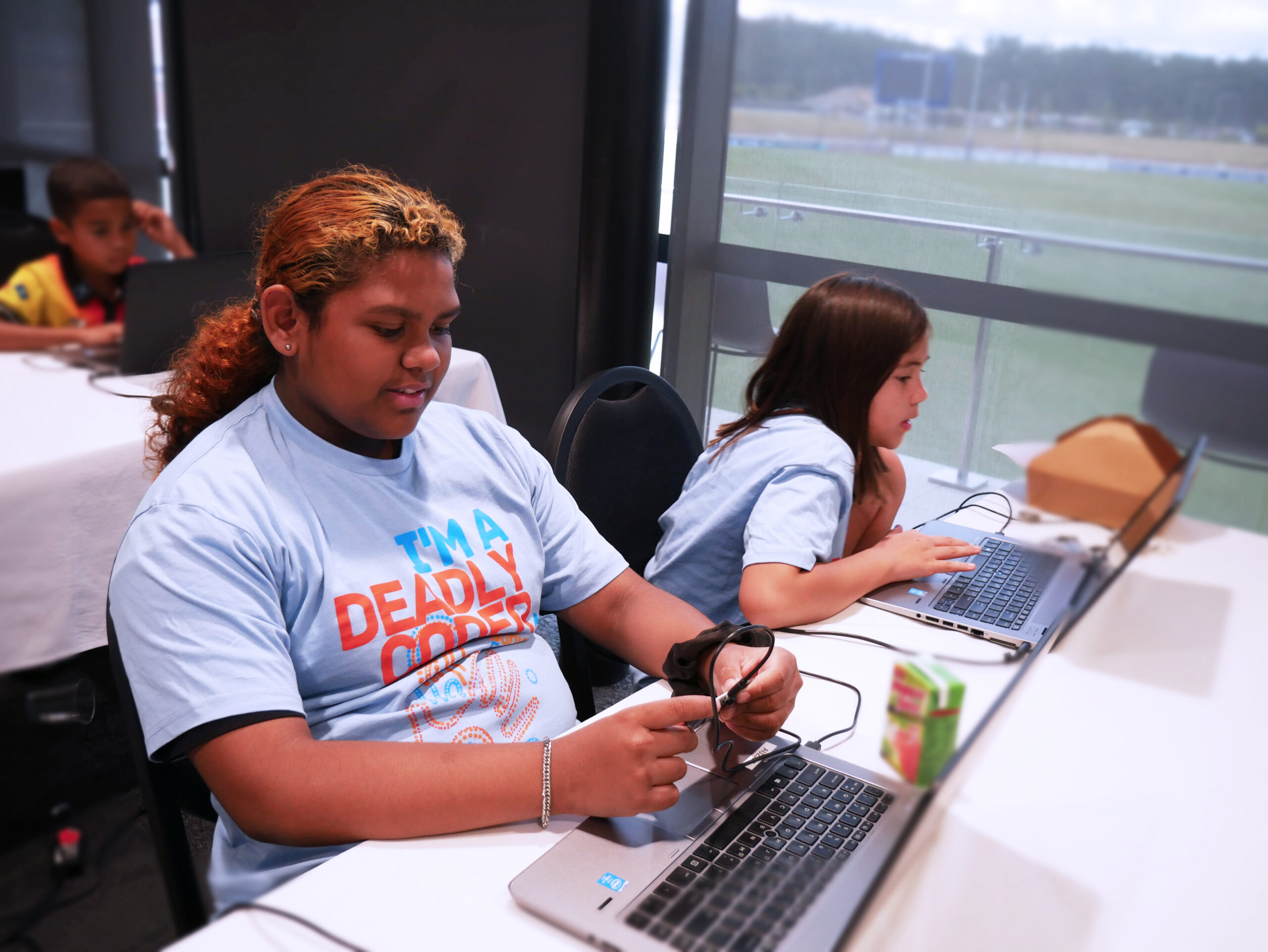 Two girls code a handheld gaming device at Brighton Homes Arena